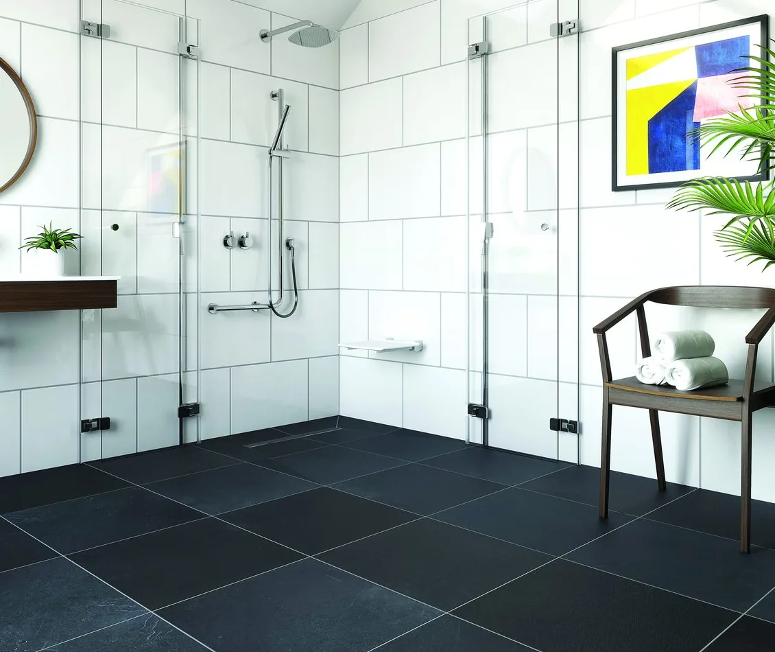 A level-access shower area with no step and a linear drain channel set into the tiled floor, with folding glass screens and a grab rail